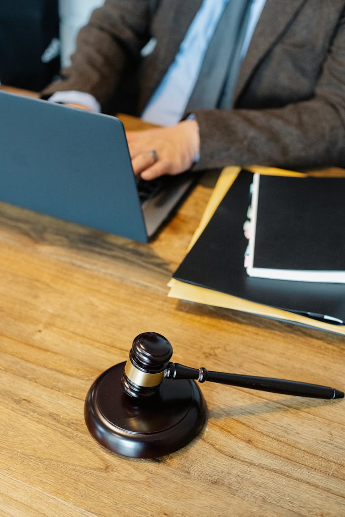 services-01 From above of crop anonymous male lawyer in formal clothes typing on laptop while sitting at wooden table with stack of documents and gavel